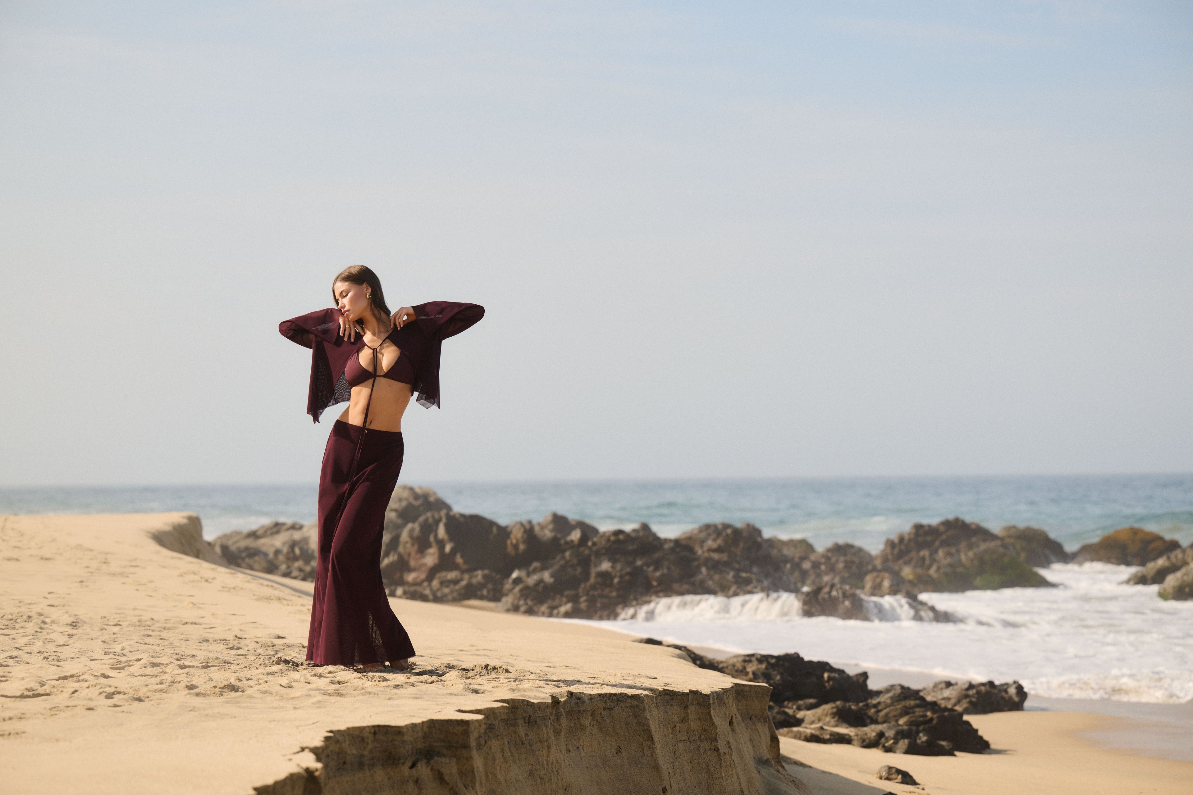 Woman in a burgundy outfit standing on a beach with ocean waves in the background